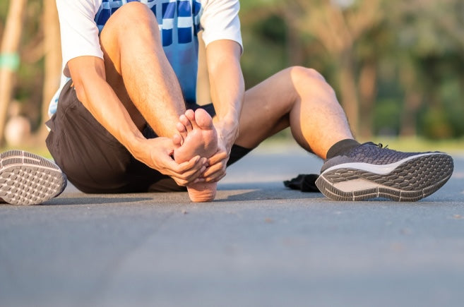 Person sitting on a road with one foot elevated, possibly experiencing arch pain.