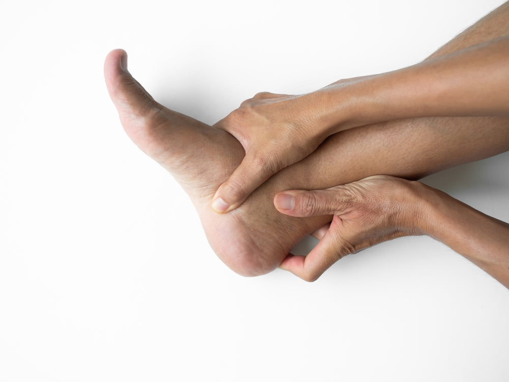 A close-up of a person's hands holding and pressing on their heel pain.