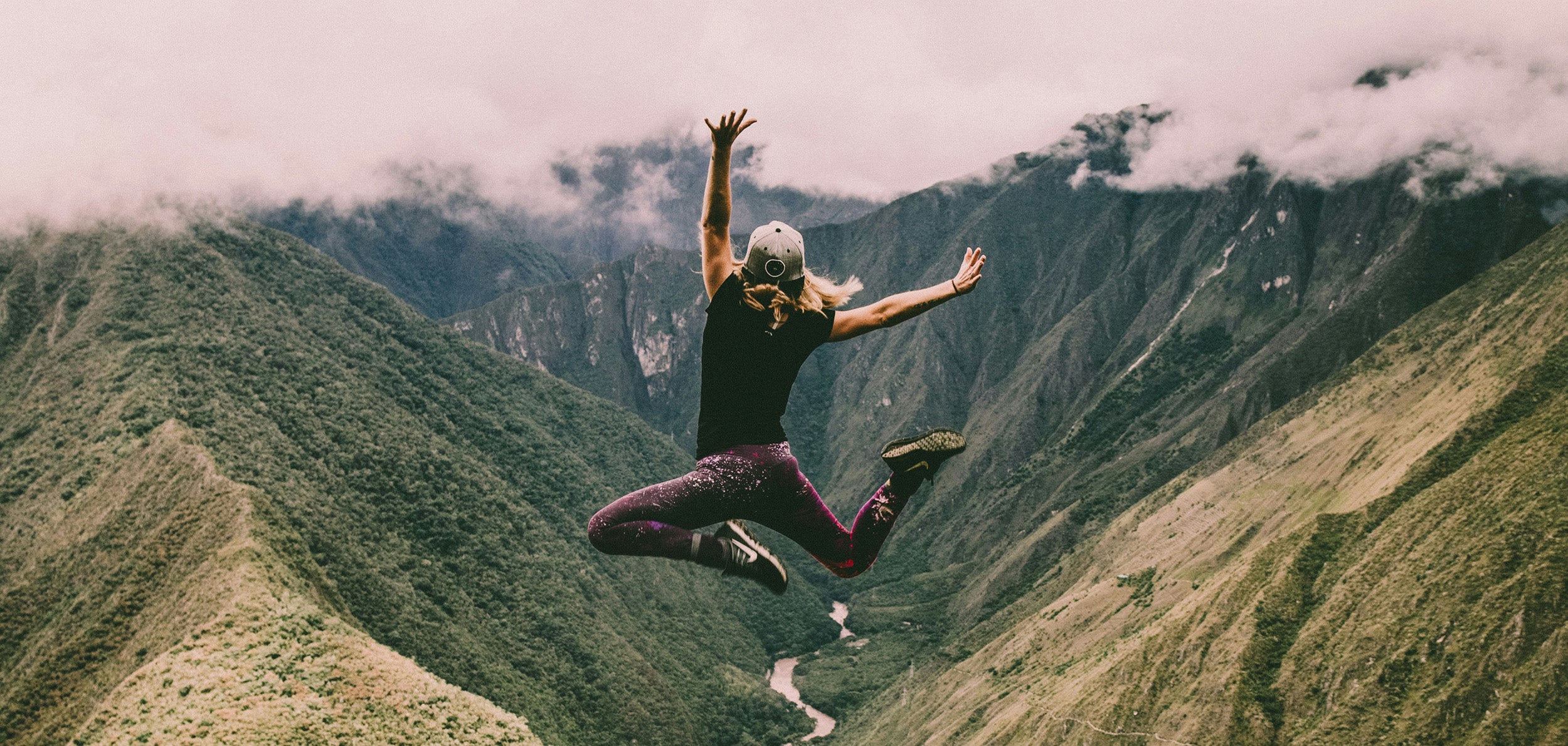 Woman in sports clothing on top of mountain, jumping in the air
