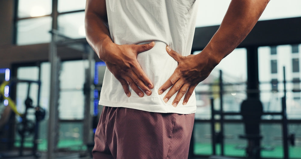 Man in a gym setting with hands on hip in pain