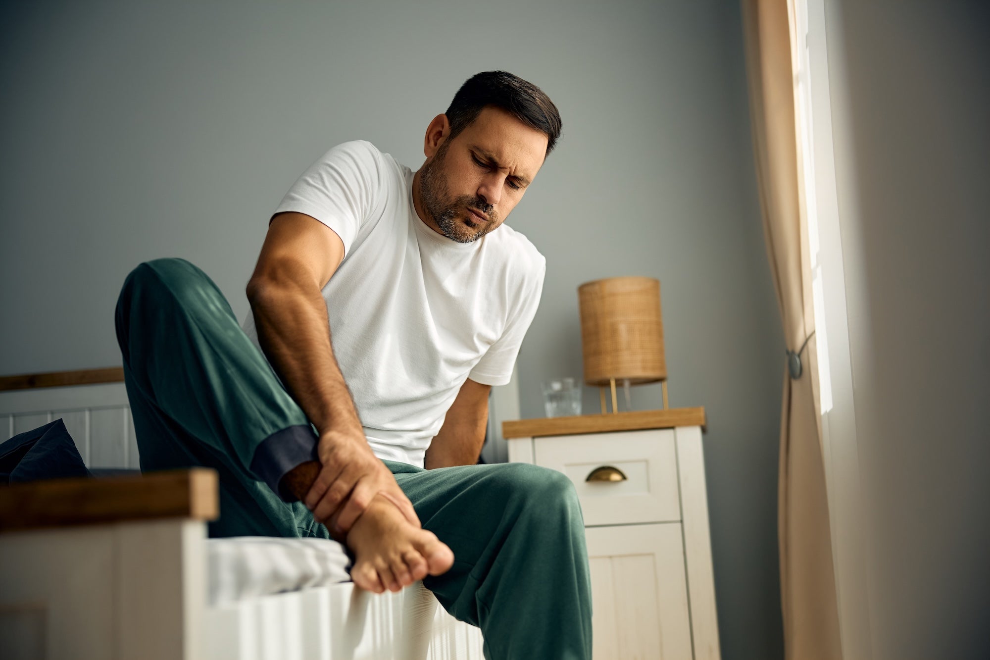 Man sitting on bed holding his foot in pain